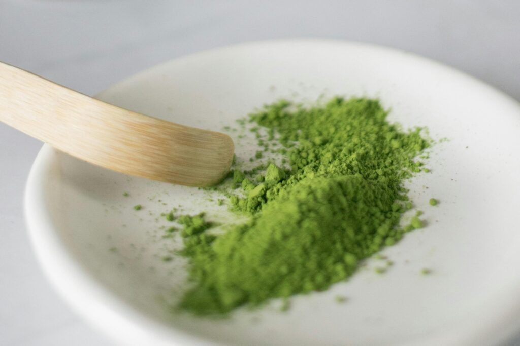 Vibrant green matcha powder on a ceramic plate with wooden spatula in a minimalist setting.