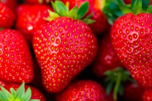 Macro shot of ripe red strawberries with green leaves, showcasing their vibrant color and texture.