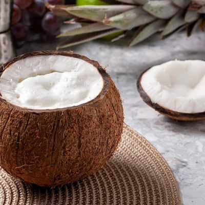A fresh coconut with foam beside a halved coconut and pineapple on a marble surface.