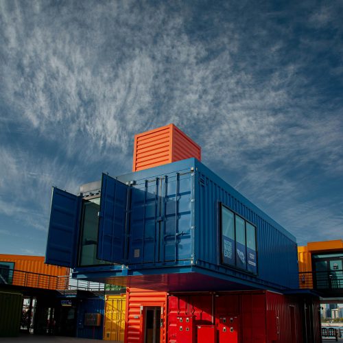 Vibrant shipping containers arranged creatively under a bright sky, showcasing modern architectural innovation.