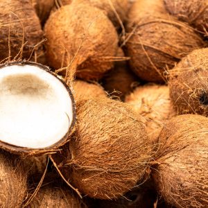 Heap of raw brown coconuts with a halved one showing the white flesh inside.